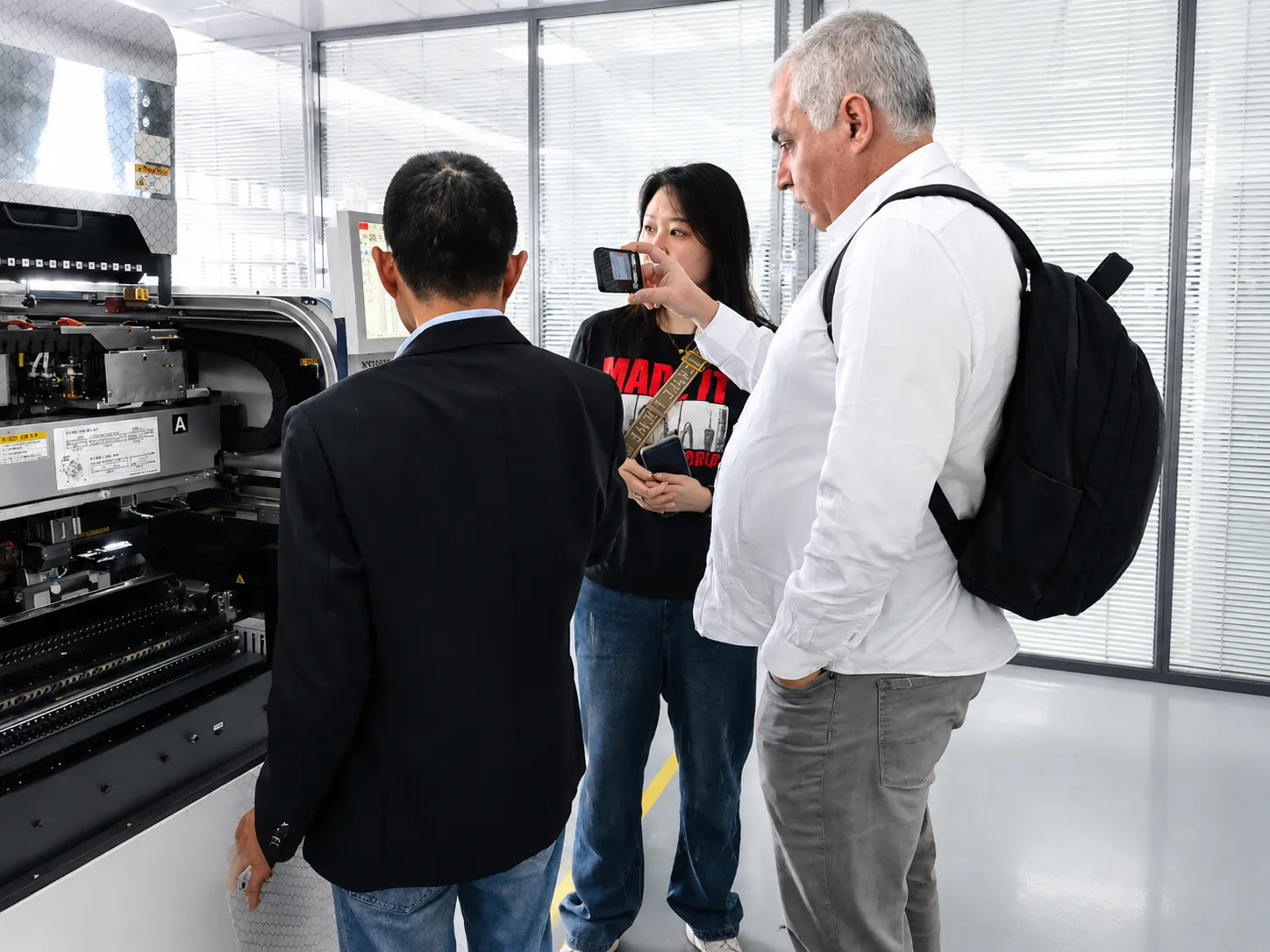 Visitors in a workshop standing beside production equipment while an operator explains the machine
