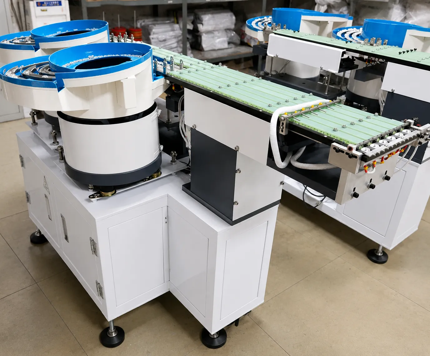 Multi-bowl vibratory lens feeder system on white cabinets, with belt transfer conveyors carrying lenses away from the bowls in a workshop