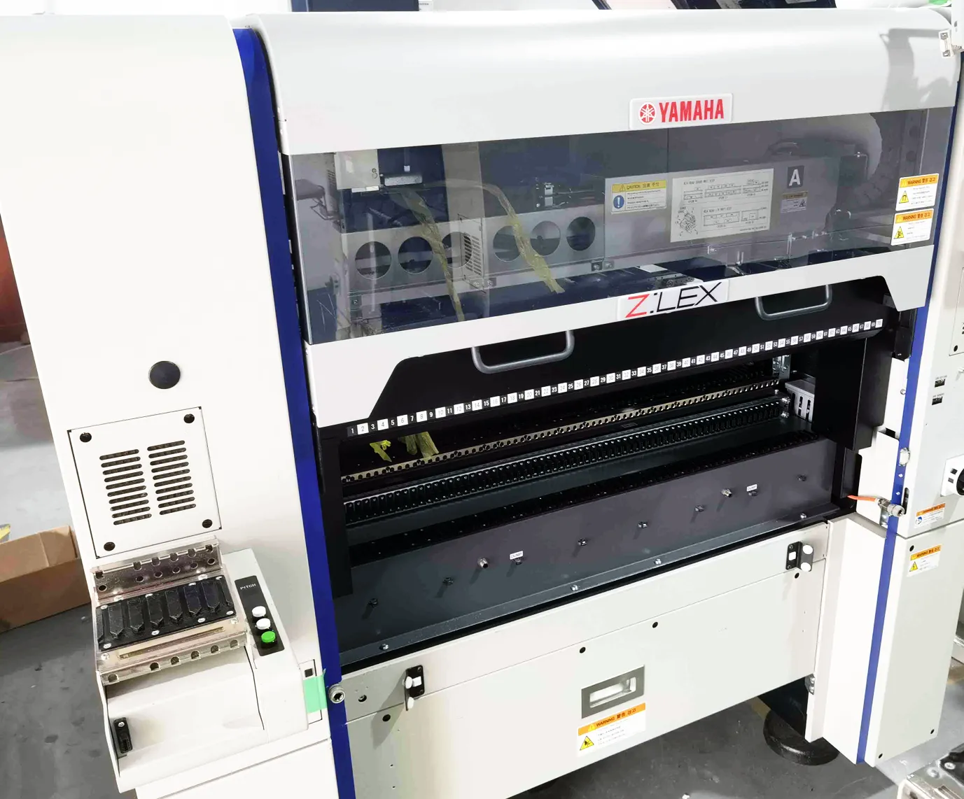 Front view of a Yamaha Z:LEX mounter with its feeder bank open and the machine still under preparation in the workshop