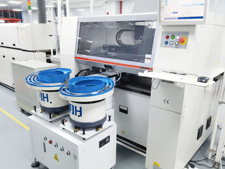 Two blue vibratory lens feeder bowls on their base beside a Hanwha pick-and-place machine